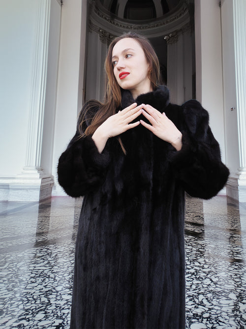 Model in black mink fur coat with hands raised, showcasing plush sleeves and elegant cut. Full-length winter coat, size M.