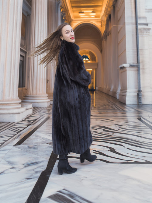 Model twirling in full-length black mink fur coat, showcasing rich texture and movement. Elegant winter outerwear, size M.