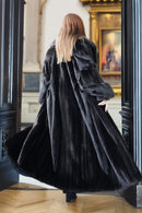 Person wearing a long black coat in an elegant interior setting