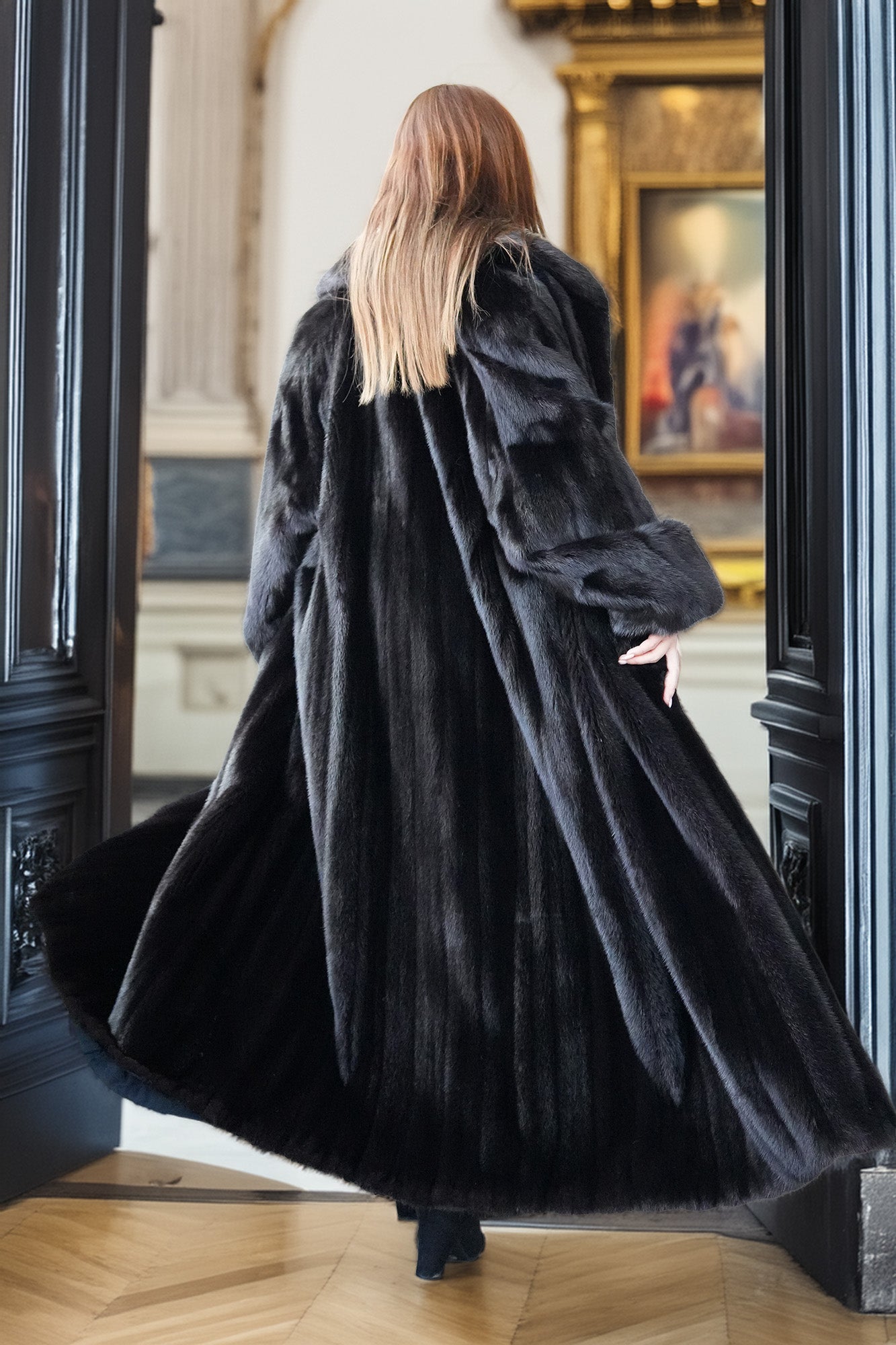 Person wearing a long black coat in an elegant interior setting