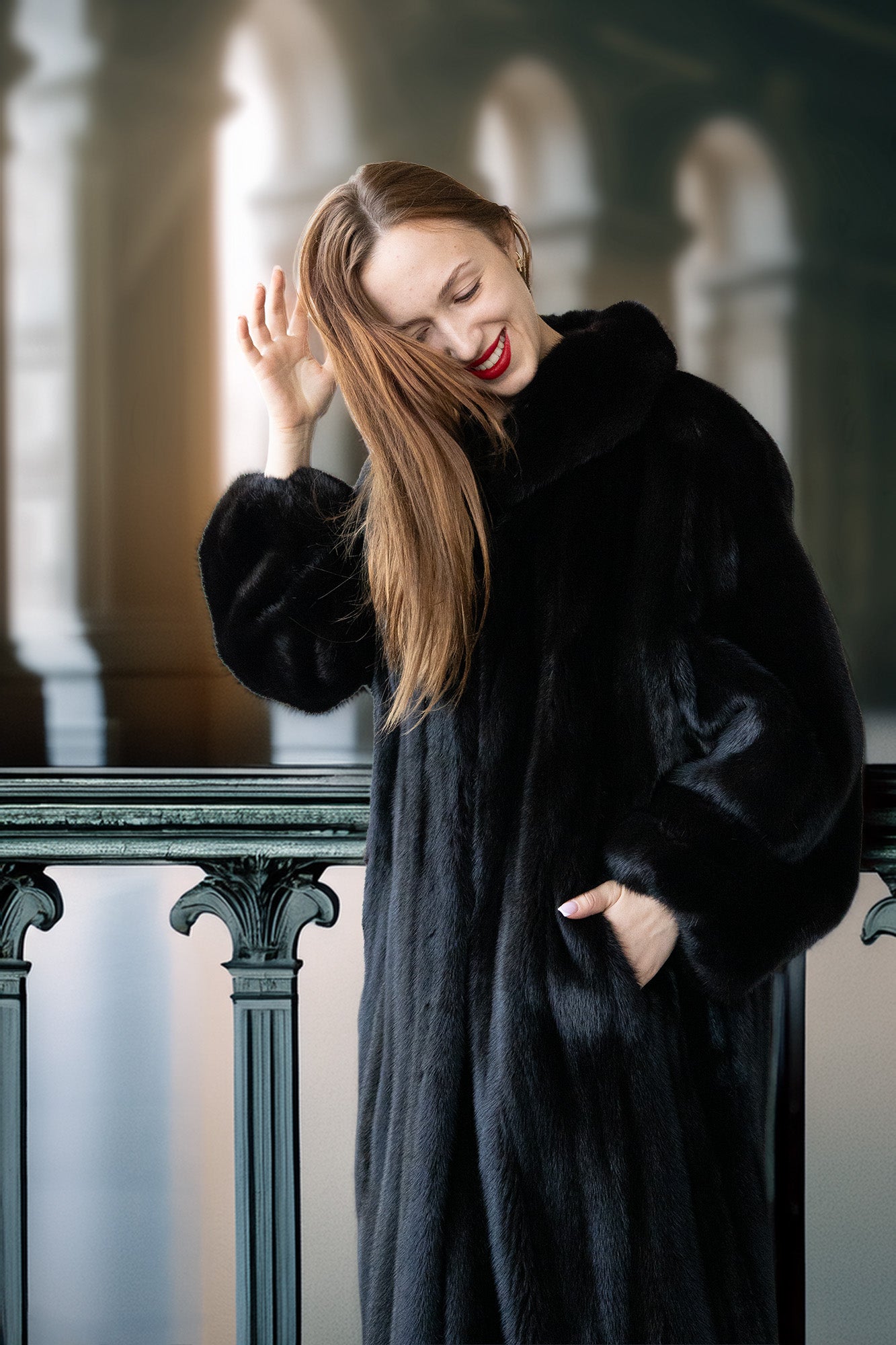 Woman in a black fur coat standing indoors with a blurred background