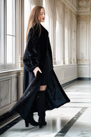 Woman wearing a long black coat in an elegant interior setting