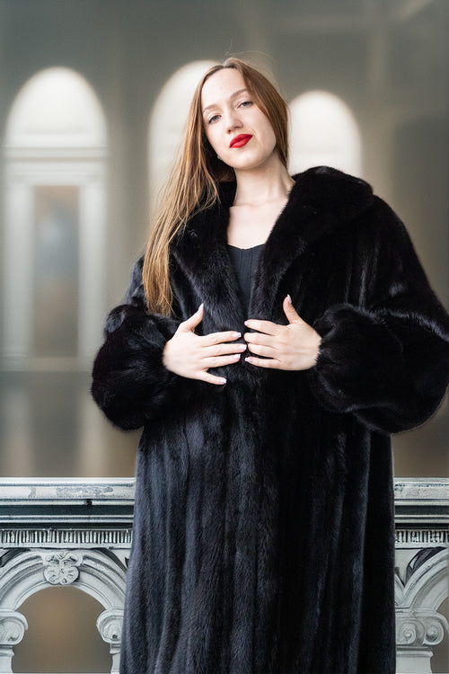 Woman wearing a black fur coat standing in front of a blurred architectural background