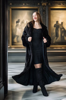 Woman in a black coat and dress standing in front of classical paintings