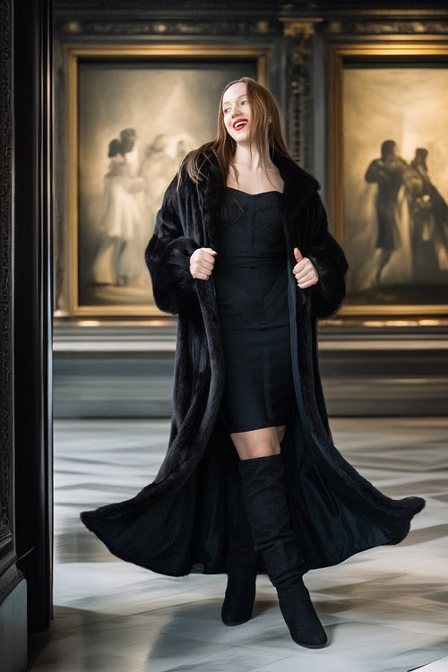 Woman in a black coat and dress standing in front of classical paintings