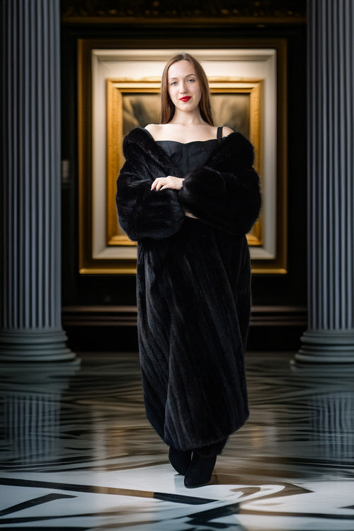 Woman in a black dress standing in a room with classical architecture and a painting in the background.