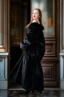 Woman in a long black fur coat standing in an ornate doorway.