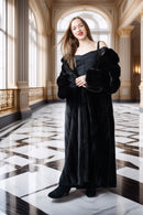 Woman in a black dress standing in an elegant interior setting with marble floors and large windows.