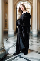 Woman in a black coat standing in an elegant interior setting with marble floors and columns.
