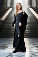 Woman in a black dress and coat standing on a marble staircase with classical columns.