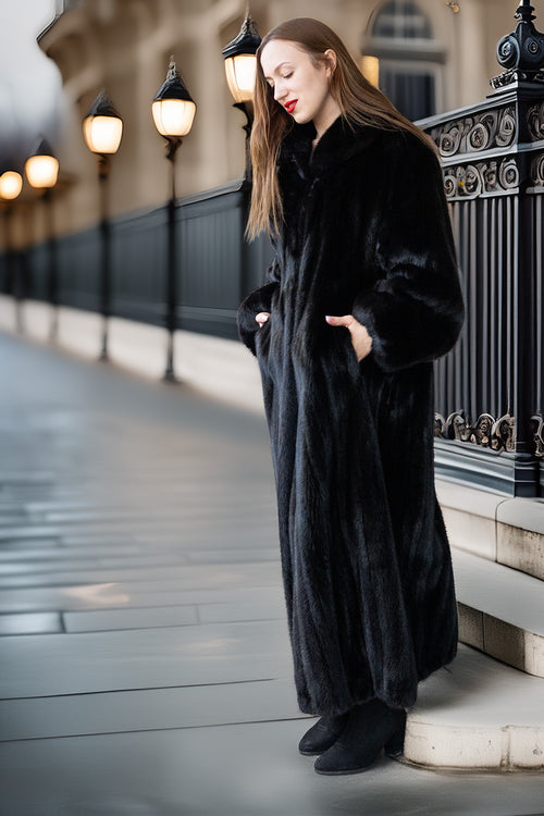 Woman wearing a long black coat standing on a city street.
