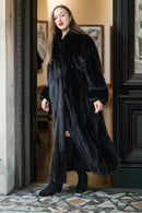 Woman wearing a long black fur coat in an elegant interior setting.