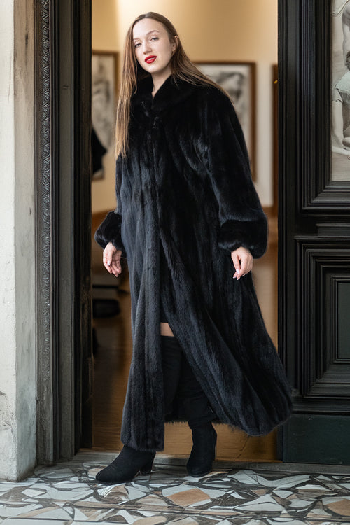 Woman wearing a long black fur coat in an elegant interior setting.