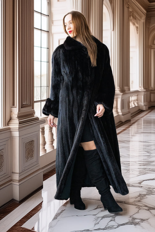 Woman in a long black fur coat standing in an elegant interior setting.