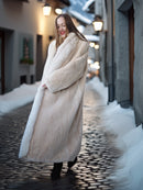 Woman in a long fur coat walking on a snowy street at night.