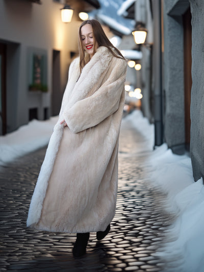 Woman in a long fur coat walking on a snowy street at night.