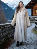 Woman in a fur coat standing in a mountainous area with a wooden cabin.