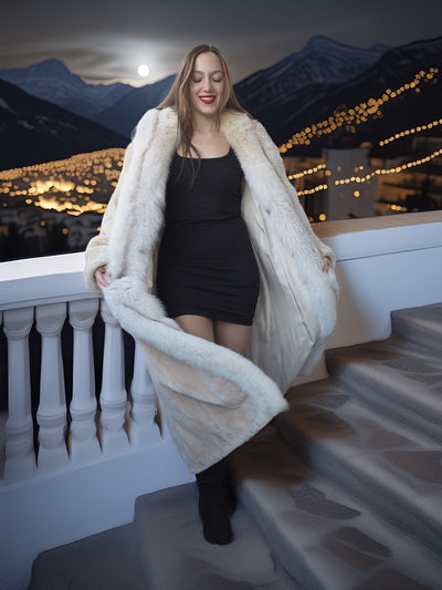 Woman in a fur coat standing on a balcony with mountains in the background
