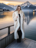 Woman in a white fur coat standing on a dock with mountains and a lake in the background