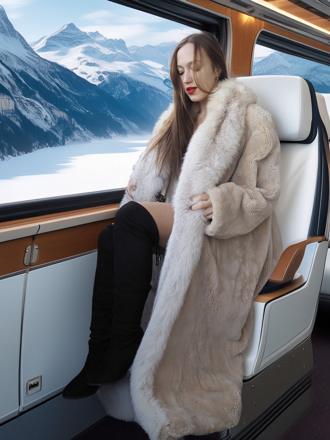 Woman in a fur coat sitting on a train with a scenic mountain view outside.