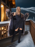 Woman in a fur coat standing on a snowy balcony with mountains in the background