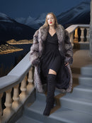 Woman in a fur coat standing on steps with a mountainous landscape in the background