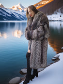 Woman in a fur coat standing by a snowy lake with mountains in the background
