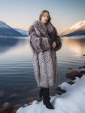 Woman in a fur coat standing by a lake with mountains in the background