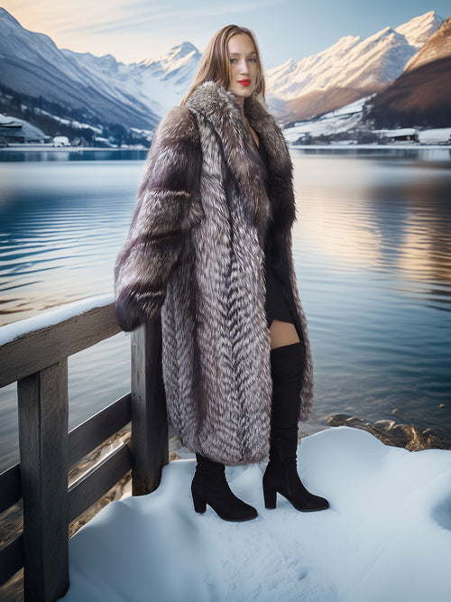 Woman in a fur coat standing by a snowy lake with mountains in the background