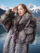 Woman in a fur coat standing in front of a mountainous landscape with a lake.