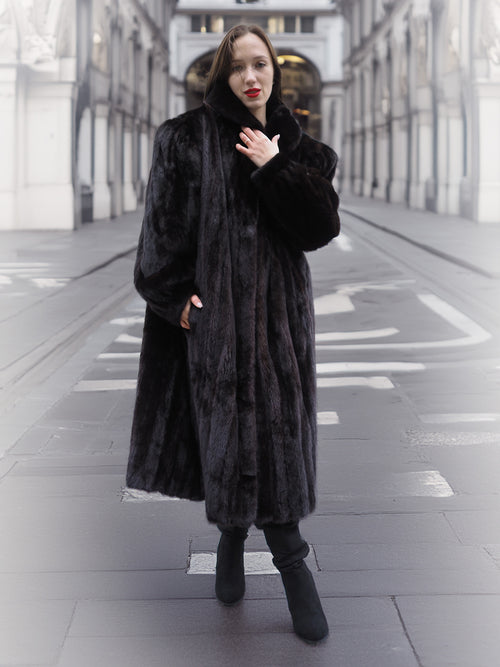 Model poses in a black mink fur coat with hands in pockets, showcasing the coat's rich texture and timeless elegance.