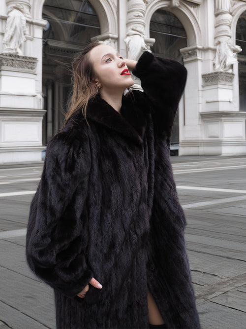 Elegant black mink fur coat with soft texture and wide collar, styled for upscale outerwear fashion in a classic architectural setting.