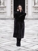 Model poses in a full-length black mink fur coat with arms crossed, showcasing its plush texture and elegant fit.