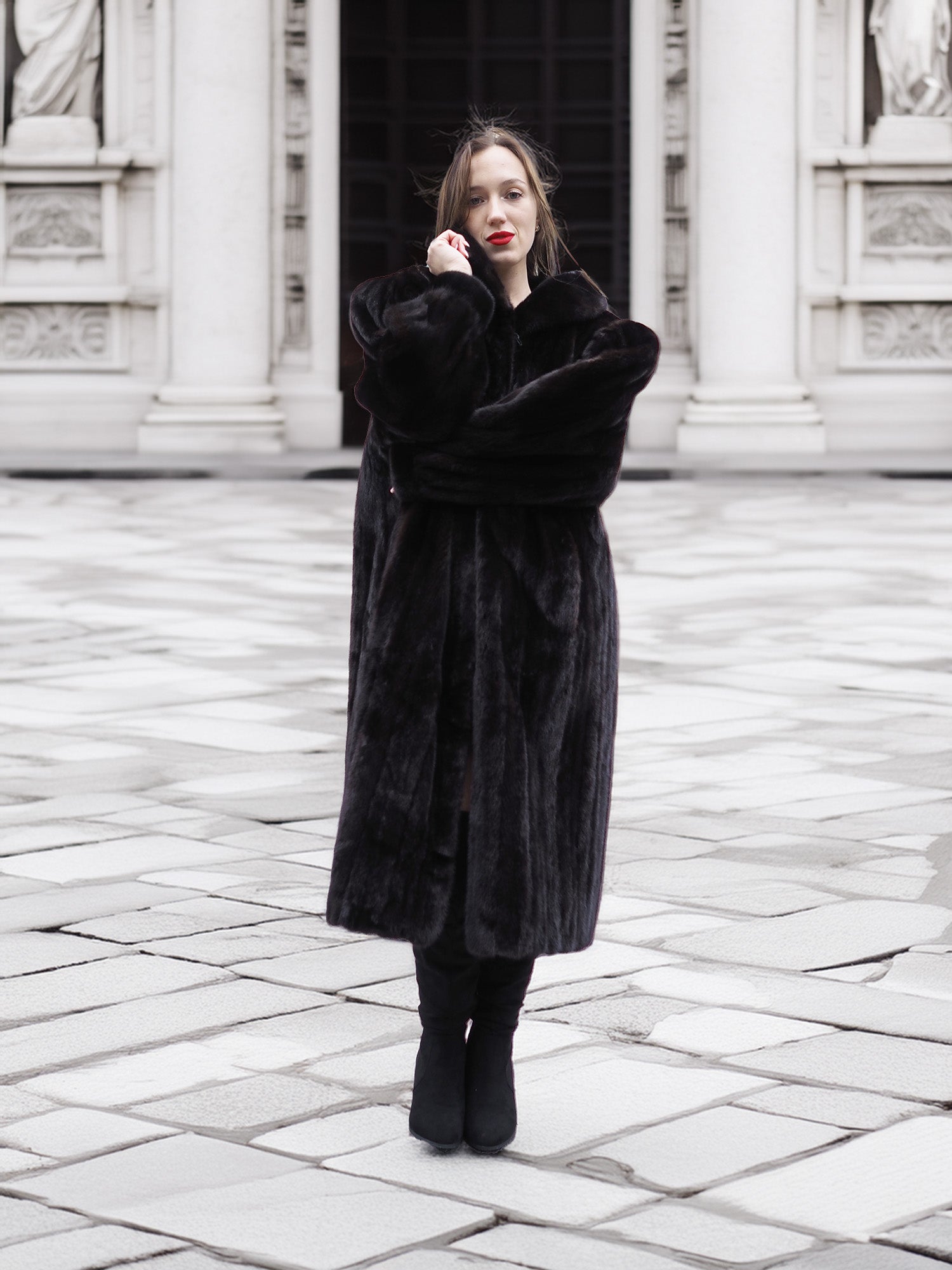 Model poses in a full-length black mink fur coat with arms crossed, showcasing its plush texture and elegant fit.