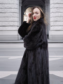 Side profile of a model in a black mink fur coat, showcasing the coat’s soft finish and elegant winter fashion appeal.