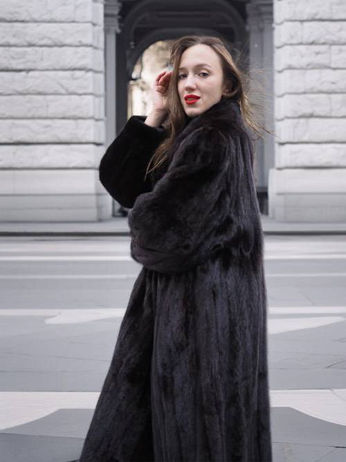 Side profile of a model in a black mink fur coat, showcasing the coat’s soft finish and elegant winter fashion appeal.