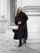 Model leans against a wall in a black mink fur coat, styled with thigh-high boots for a modern luxury look.