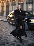 Woman in a long black coat standing on a city street with a car in the background