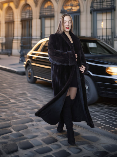 Woman in a long black coat standing on a city street with a car in the background