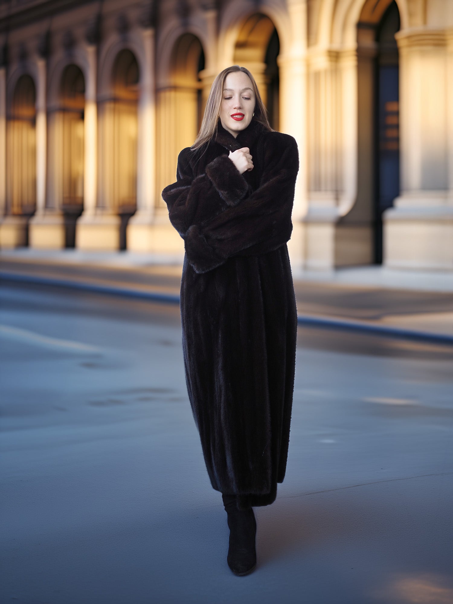Woman in a long black coat standing in front of a building with arches.