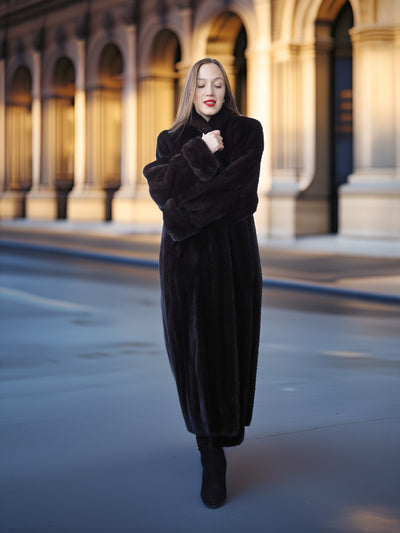Woman in a long black coat standing in front of a building with arches.