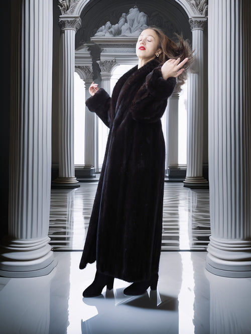 Woman in a long black coat standing in a classical architectural setting with columns.