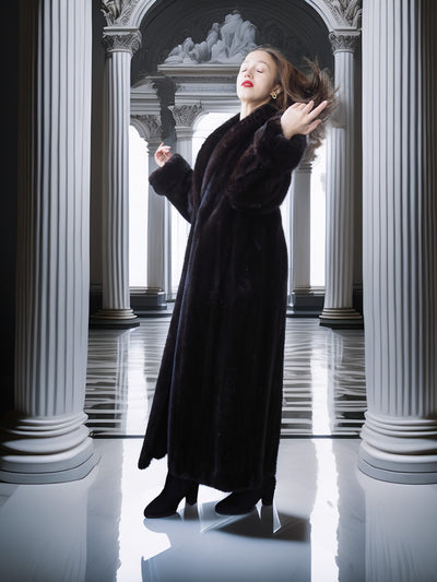 Woman in a long black coat standing in a classical architectural setting with columns.