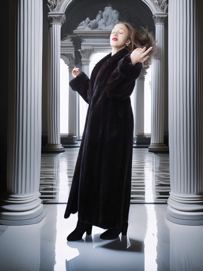 Woman in a long black coat standing in a classical architectural setting with columns.
