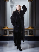 Woman wearing a long black fur coat in an elegant interior setting.