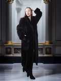 Woman wearing a long black fur coat in an elegant interior setting.