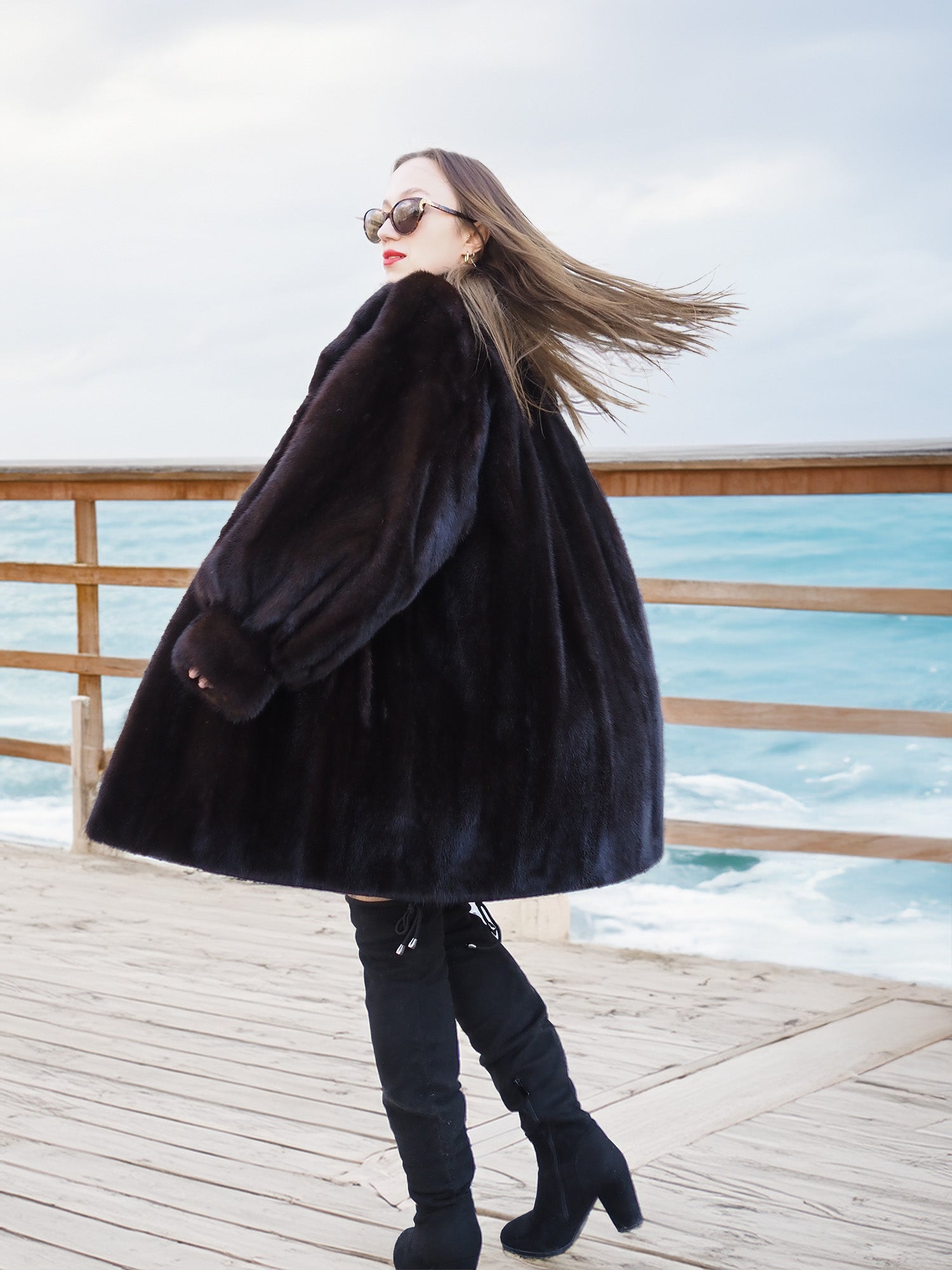 Black Mink Swing Coat - Riviera Noir flared open with a scenic coastal town view. Elegant mink outerwear for winter fashion lovers.