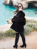 Black Mink Swing Coat - Riviera Noir in motion with a scenic ocean backdrop. Elegant and warm fur coat for luxury winter wear.