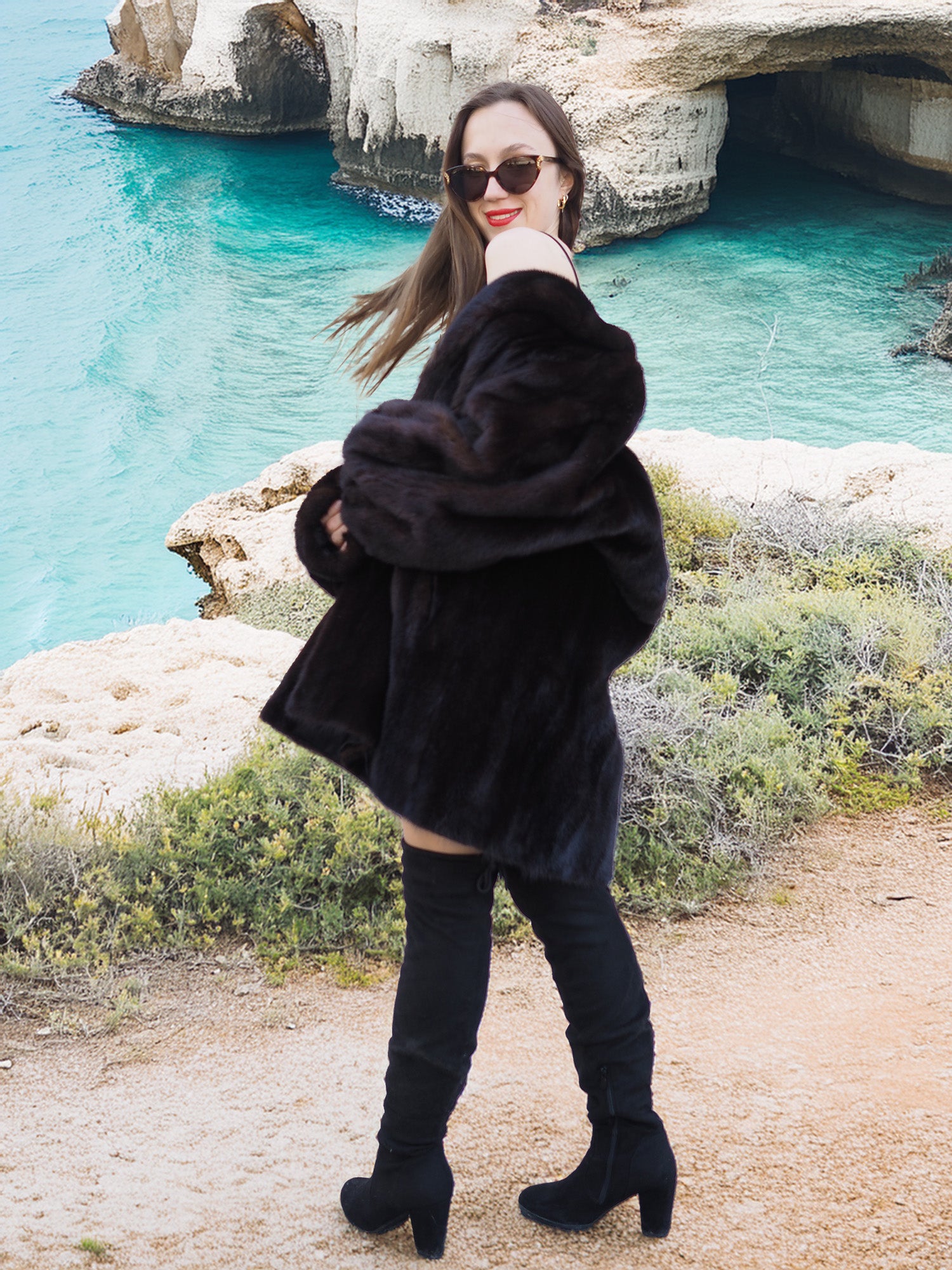 Black Mink Swing Coat - Riviera Noir in motion with a scenic ocean backdrop. Elegant and warm fur coat for luxury winter wear.