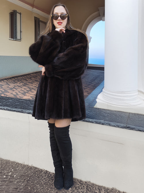 Black Mink Swing Coat - Riviera Noir styled with thigh-high boots near a columned building. Elegant mink outerwear for winter fashionistas.